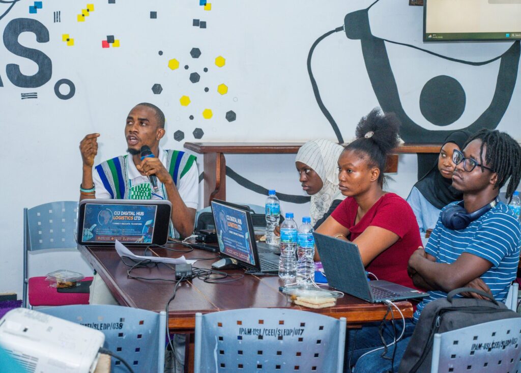 Founder Chernor I. Jalloh speaking to participants at a workshop table with laptops